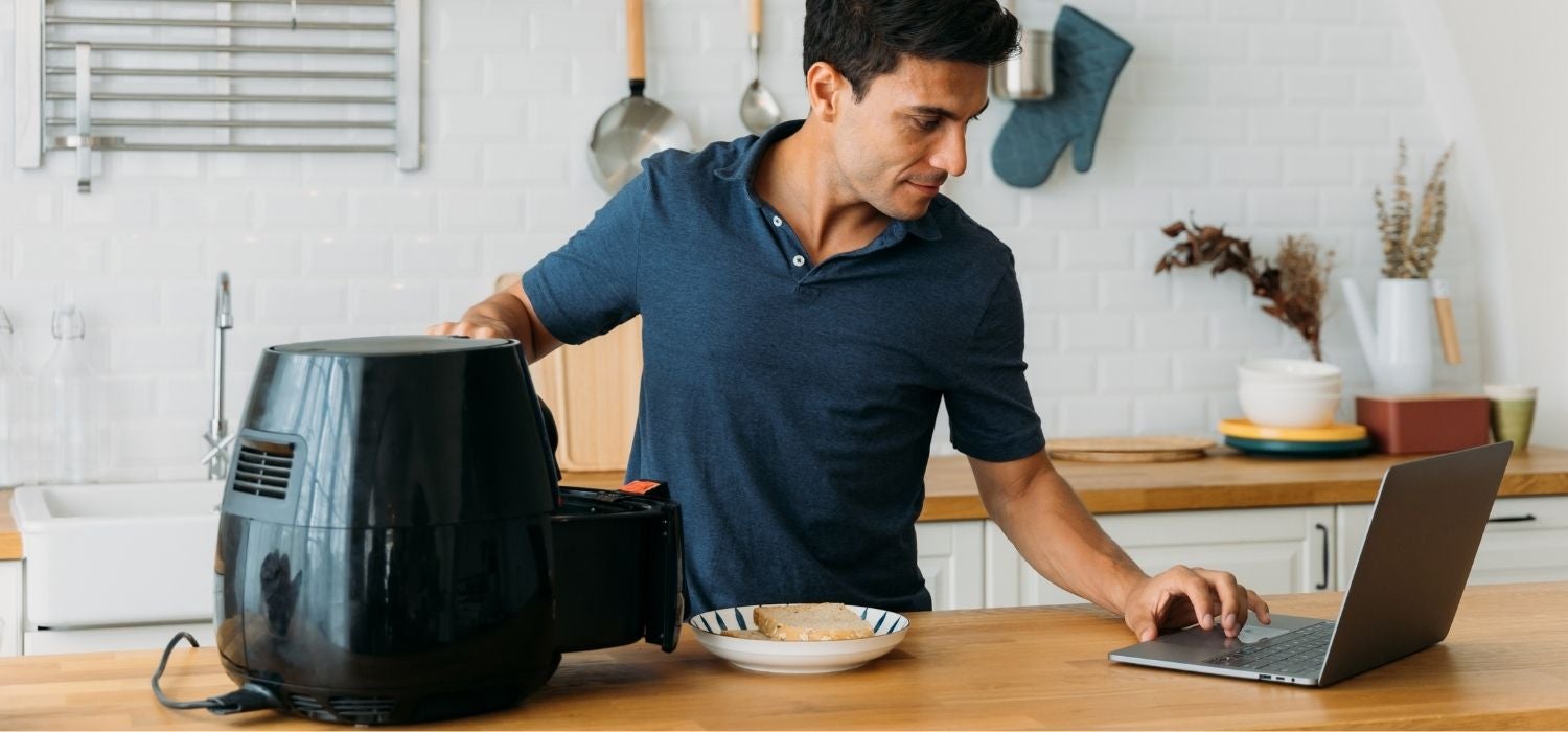 Mann benutzt Airfryer in der Küche mit Laptop für das Rezept