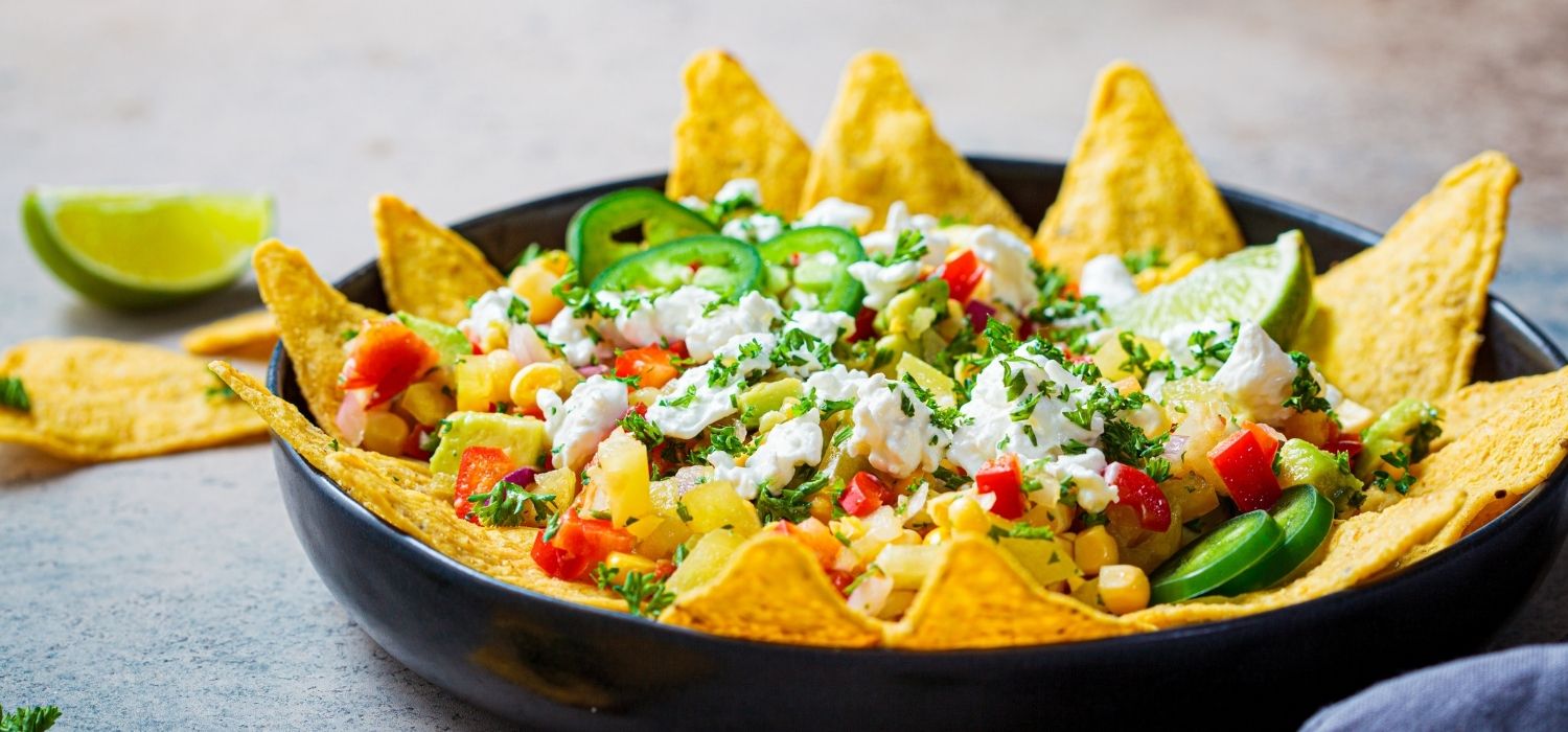 Mexikanischer Taco-Salat mit Käse, Paprika und Mais garniert mit weiterem Gemüse und Limette serviert in einer Schüssel.