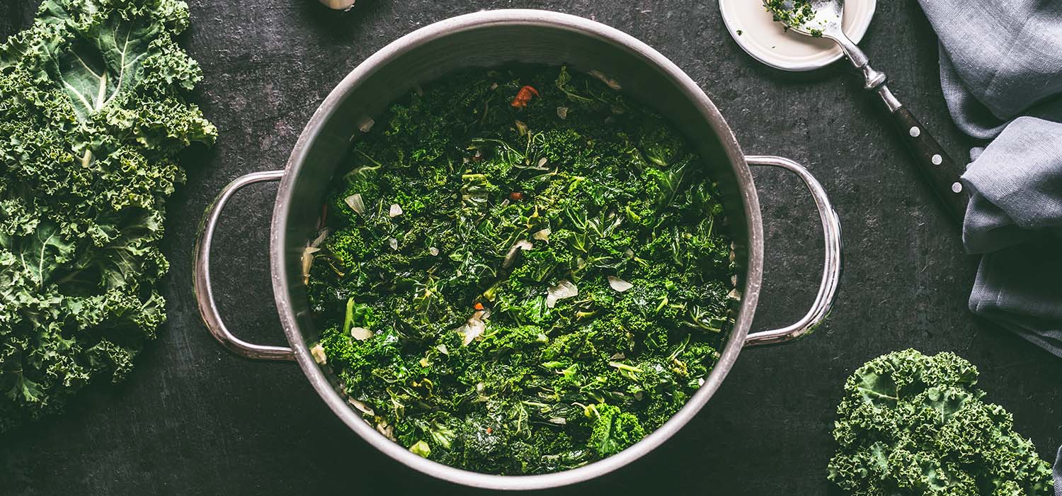 Grünkohl in einem Topf neben einer Knoblauchzehe und Walnüssen.