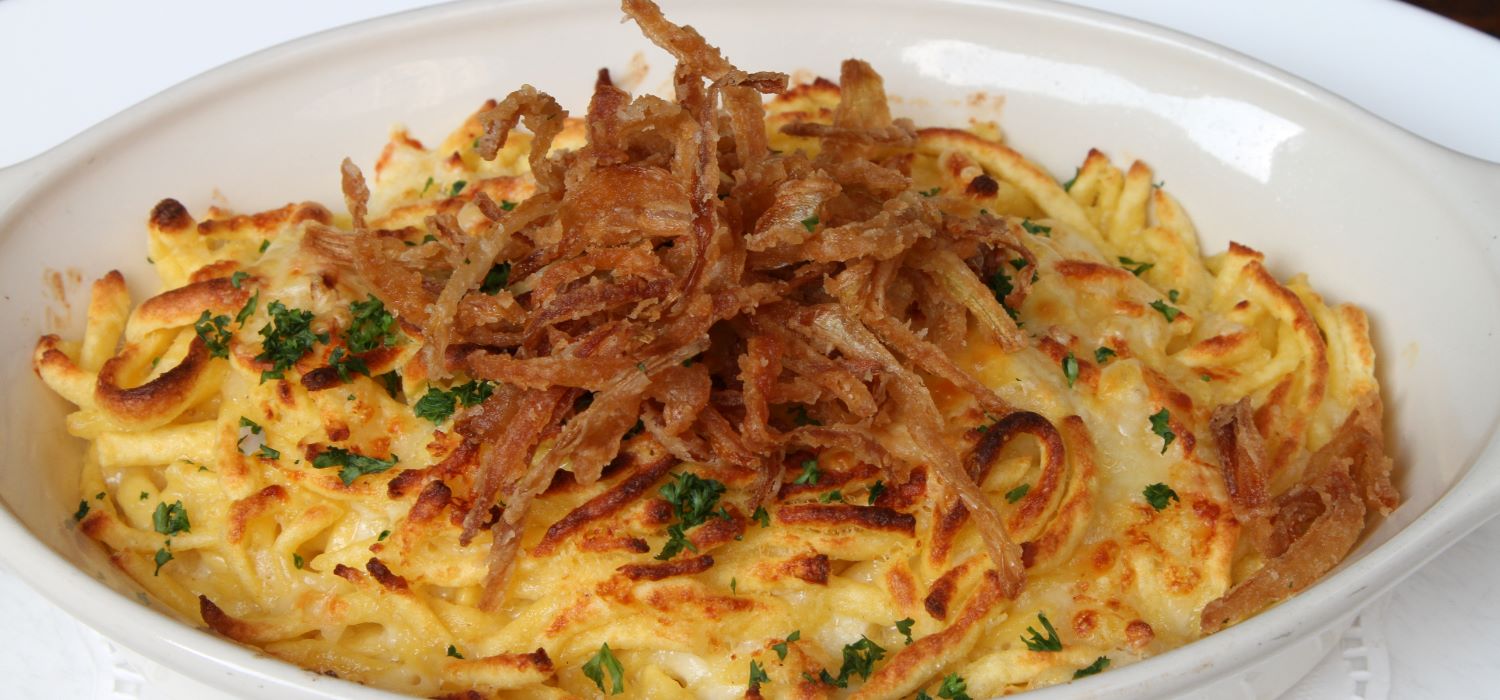 Käsespätzle mit Röstzwiebeln garniert mit Kräutern serviert in einer Auflaufform.