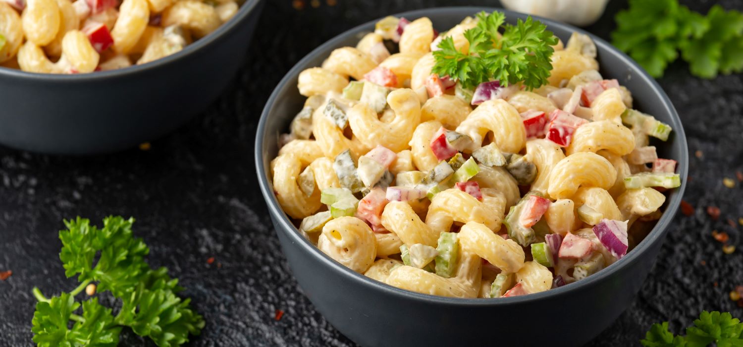 Nudelsalat mit Paprika, Zwiebel und Gürkchen in Mayonnaise Dressing in einer Schüssel.