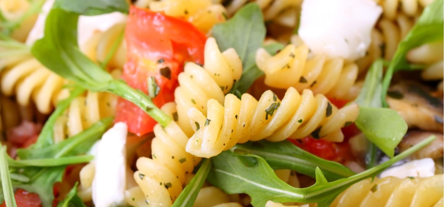 Nudelsalat mit Gemüse und Dressing in einer Schüssel serviert.