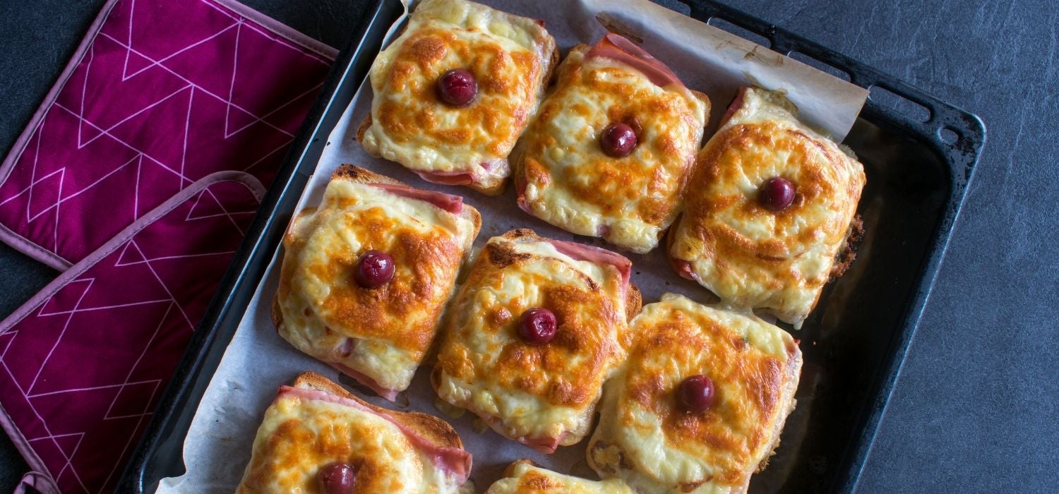 Toast Hawaii garniert mit einer Kirsche serviert auf einem Backblech mit Backpapier.